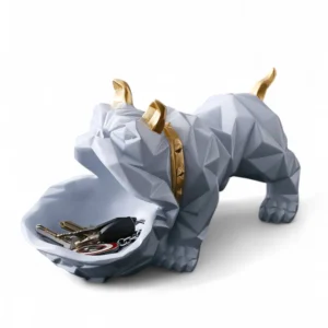 The Geometric Bulldog Key & Accessory Holder from DNF Ceramics is where art meets functionality. Crafted in a striking polygonal design, this decorative bulldog figurine brings a contemporary aesthetic to your home or office. With its open mouth serving as a practical tray, it’s ideal for holding everyday essentials like keys, coins, jewelry, or small accessories. The sleek grey finish, accented with gold detailing on the horns and collar, adds a luxurious touch, making it a standout décor piece for modern interiors. Beyond its utility, the bulldog symbolizes loyalty and strength — adding character and meaning to your space. Perfect for entryway tables, office desks, or as a stylish gift for pet and design lovers alike. Features: Handcrafted with durable resin in a modern geometric form Functional tray for keys, coins, or small items Elegant grey body with metallic gold accents Perfect for tabletops, consoles, or gifting Blends contemporary style with playful charm