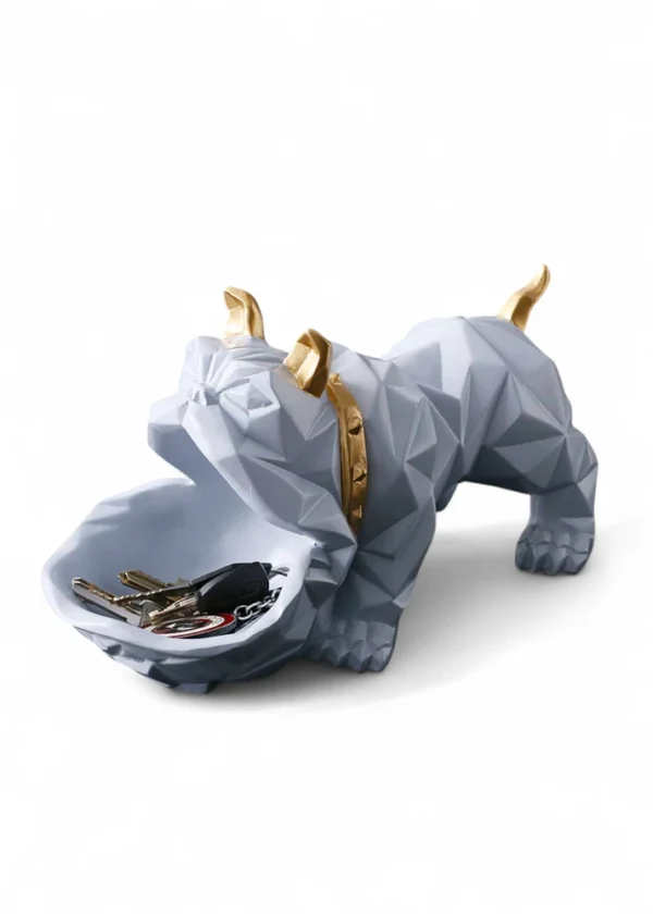 The Geometric Bulldog Key & Accessory Holder from DNF Ceramics is where art meets functionality. Crafted in a striking polygonal design, this decorative bulldog figurine brings a contemporary aesthetic to your home or office. With its open mouth serving as a practical tray, it’s ideal for holding everyday essentials like keys, coins, jewelry, or small accessories. The sleek grey finish, accented with gold detailing on the horns and collar, adds a luxurious touch, making it a standout décor piece for modern interiors. Beyond its utility, the bulldog symbolizes loyalty and strength — adding character and meaning to your space. Perfect for entryway tables, office desks, or as a stylish gift for pet and design lovers alike. Features: Handcrafted with durable resin in a modern geometric form Functional tray for keys, coins, or small items Elegant grey body with metallic gold accents Perfect for tabletops, consoles, or gifting Blends contemporary style with playful charm