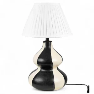 The Monochrome Wave Ceramic Table Lamp from DNF Ceramics redefines minimalism with a sculptural twist. Crafted by skilled artisans, its fluid gourd-shaped form is hand-painted in contrasting black and ivory tones that flow in wavy symmetry — an artistic statement that stands out in any room. Topped with a crisp white pleated lampshade, this lamp diffuses light softly, highlighting the smooth ceramic finish while adding warmth to your interiors. The design blends effortlessly with both contemporary and classic spaces, offering a refined yet eye-catching centerpiece for your home. Whether placed beside your bed, on a console, or in your living room, this monochrome masterpiece brings artful sophistication and handcrafted beauty to your décor. Features: Handcrafted black and white ceramic base with artistic wave design Elegant gourd silhouette for sculptural appeal White pleated shade for diffused, ambient lighting Perfect for modern, minimal, or art-inspired spaces Made by artisans at DNF Ceramics with premium craftsmanship