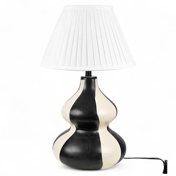 The Monochrome Wave Ceramic Table Lamp from DNF Ceramics redefines minimalism with a sculptural twist. Crafted by skilled artisans, its fluid gourd-shaped form is hand-painted in contrasting black and ivory tones that flow in wavy symmetry — an artistic statement that stands out in any room. Topped with a crisp white pleated lampshade, this lamp diffuses light softly, highlighting the smooth ceramic finish while adding warmth to your interiors. The design blends effortlessly with both contemporary and classic spaces, offering a refined yet eye-catching centerpiece for your home. Whether placed beside your bed, on a console, or in your living room, this monochrome masterpiece brings artful sophistication and handcrafted beauty to your décor. Features: Handcrafted black and white ceramic base with artistic wave design Elegant gourd silhouette for sculptural appeal White pleated shade for diffused, ambient lighting Perfect for modern, minimal, or art-inspired spaces Made by artisans at DNF Ceramics with premium craftsmanship
