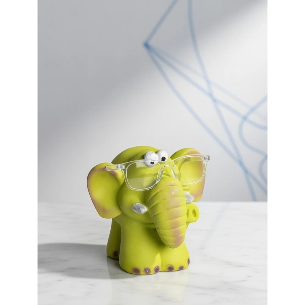 The Smarty Elephant Glasses Holder is a fun and functional tabletop accessory that blends charm with practicality. Designed in a bright lime-green finish with soft pastel detailing on the ears and feet, this adorable elephant features a sturdy trunk and face structure that securely holds eyeglasses when not in use. Its expressive eyes and cute sculpted details give it a lively personality, making it perfect for desks, bedside tables, study corners, kids’ rooms, and office décor. Beyond being a simple glasses stand, it doubles as a decorative showpiece that instantly adds character to any space. Smarty Elephant Glasses Holder